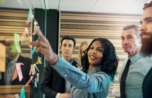 Businesswoman leading collaboration session with postit note board, possibly engaging the Board and CEO.